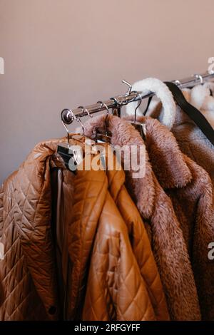 Brown beige women's clothes hanging on a hanger in a row. Autumn winter fashion set. Fur coat collection Stock Photo