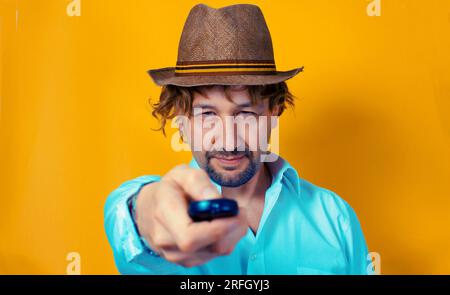 Expressive young man on a yellow background using a remote control , channel hoping concept , switching on a tv set , portrait . Stock Photo