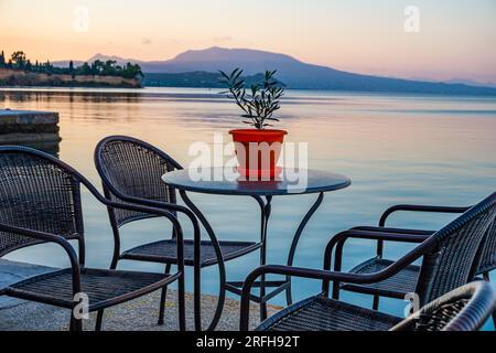 Beautiful decorated table with a colorful flower pot by the sea coast at Koroni and a wonderful view of the Messenian gulf. Koroni, Messenia, Greece. Stock Photo