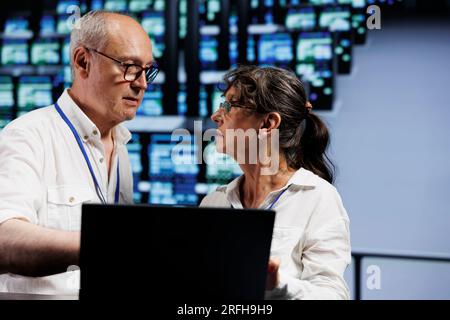 Certified aged developers working to maintain uptime in high tech facility. Trained IT programmers brainstorming solutions to data center server cabinets crashing, trying to fix components Stock Photo