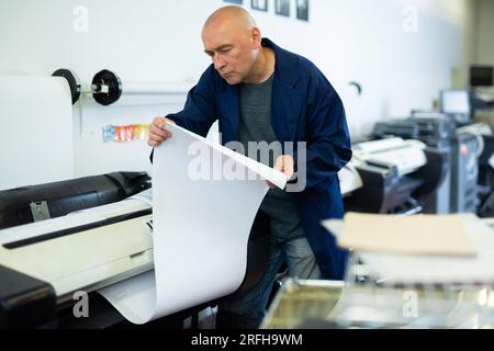 Service man uses plotter and checks functionality in printing shop Stock Photo