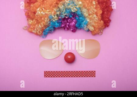 Funny Party concept face formed with glasses lens. Rainbow Clown Wig Set and red clown nose like a face, Fluffy Afro Synthetic Cosplay Anime Fancy Wig Stock Photo