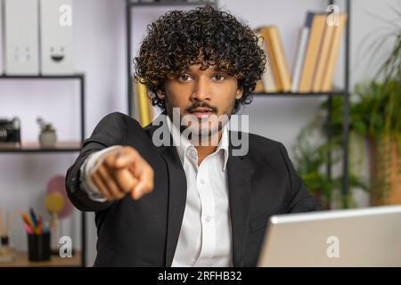 I choose you. Young indian businessman programmer software developer working on office laptop pointing to camera, looking with happy expression, making choice, showing direction. Arab freelancer man Stock Photo