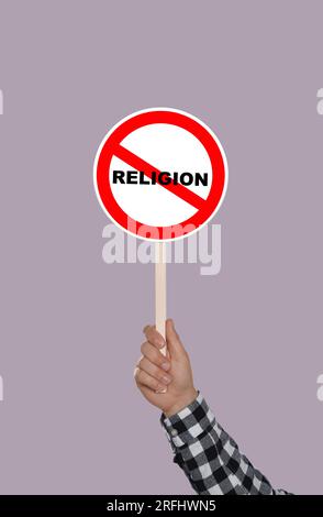 Atheism concept. Man holding prohibition sign with crossed out word Religion on color background Stock Photo