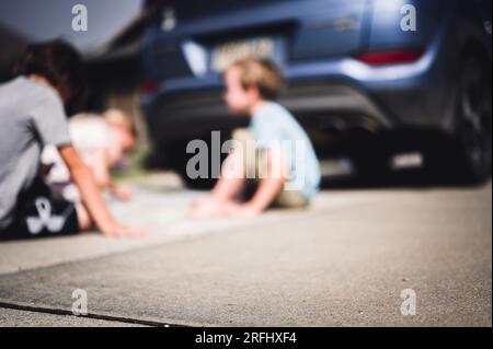 Children sitting on a driveway behind a vehicle in a blind spot out of view of the driver.  Stock Photo