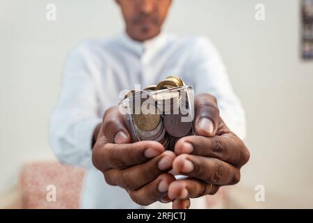 A man holds a glass filled with Indian rupees coins. The coins are of various denominations and colors Stock Photo