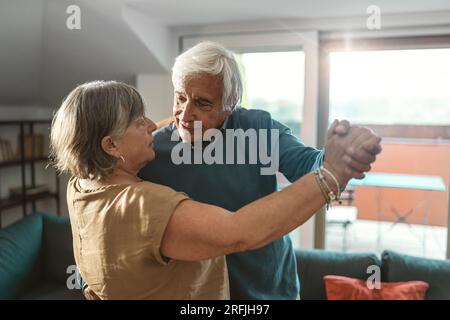 A lovely scene of a married couple in their seventies sharing an intimate dance (tango, waltz or another type of partner dance) in the living room of Stock Photo