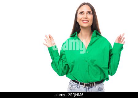 portrait of a smart pensive slim cute brown-eyed brunette woman dressed in a green shirt smiling on a white background with copy space Stock Photo