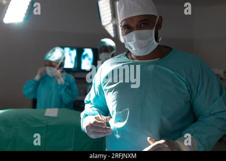 Portrait of biracial male surgeon wearing surgical gown in operating ...