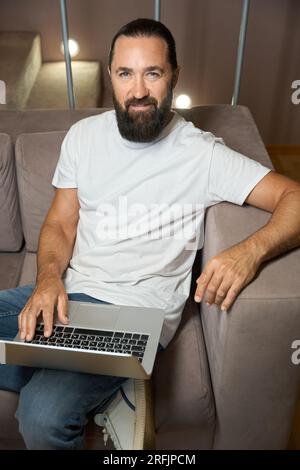 Handsome man sits on a sofa with a laptop Stock Photo