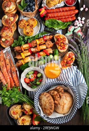 Various of grilled meal - grilled meats, vegetables, fruits, salad and potatoes on a dark wooden background. Top view. Stock Photo