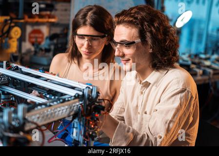 Young man and woman in protective glasses doing experiments in robotics in a laboratory. Robot on the table Stock Photo