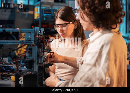 Young man and woman in protective glasses doing experiments in robotics in a laboratory. Robot on the table Stock Photo