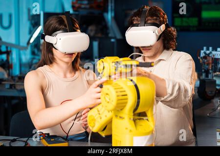 Young man and woman in VR glasses doing experiments in robotics in a laboratory. Robot on the table Stock Photo