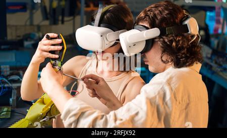 Young man and woman in VR glasses doing experiments in robotics in a laboratory. Robot on the table Stock Photo