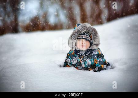 cute caucasian boy in warm winther jacker with fur hoody laying in snow in countryside on winter day. High quality photo Stock Photo