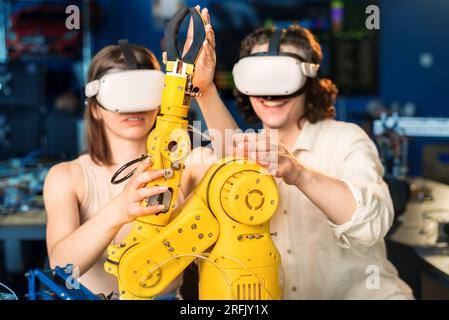 Young man and woman in VR glasses doing experiments in robotics in a laboratory. Robot on the table Stock Photo
