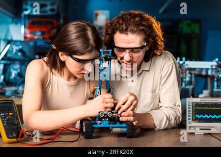 Young man and woman in protective glasses doing experiments in robotics in a laboratory. Robot and tools on the table Stock Photo