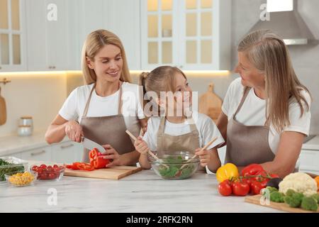 Three generations. Happy grandmother, her daughter and granddaughter cooking together in kitchen Stock Photo