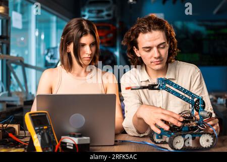 Young man and woman in protective glasses doing experiments in robotics in a laboratory using a computer. Robot and tools on the table Stock Photo