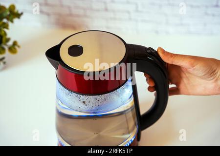 https://l450v.alamy.com/450v/2rfk5tp/a-modern-electric-kettle-with-boiling-water-and-a-a-womans-hand-pressing-the-off-button-kitchen-accessories-top-side-view-2rfk5tp.jpg