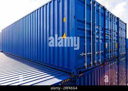 Blue cargo containers are stacked in the storage area under bright cloudy sky Stock Photo