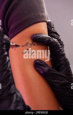 Hands of professional tattoo artist creating inscriptions on arm of woman Stock Photo