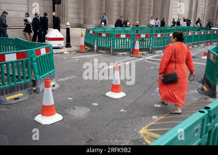 A woman whose clothing matches the colour of traffic cones crosses Threadneedle Street outside the Bank of England where extensive ongoing roadworks are causing disruption to pedestrans and traffic in the City of London, the capital's financial district, on 3rd August 2023, in London, England. Stock Photo