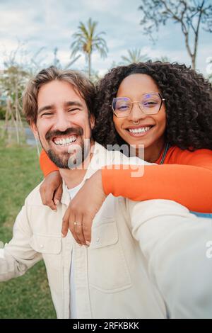 Vertical portrait of young adult multiracial couple smiling and having fun taking a selfie portrait together. Handsome boyfriend shooting a picture with his happy girlfriend. Real relationship. High quality photo Stock Photo