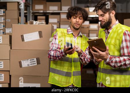 Delivery logistic business. Two male warehouse workers looking photos using mobile phone Stock Photo