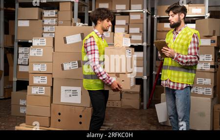 Warehouse manager using digital tablet doing inventory and courier with boxes preparing goods for shipment Stock Photo