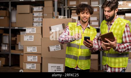Warehouse manager and foreman working together in a large warehouse looking at smartphone Stock Photo