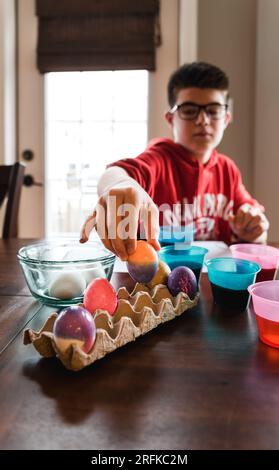 Boy placing colorful dyed easter egg in a cardboard carton to dry. Stock Photo
