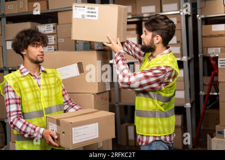 Two mixed race warehouse workers preparing a shipment in a large warehouse. Logistics employees working in warehouse in a large distribution center. Stock Photo