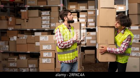 Two warehouse mixed race workers using a digital tablet while recording inventory and preparing shipment. Logistics employees working with warehouse Stock Photo