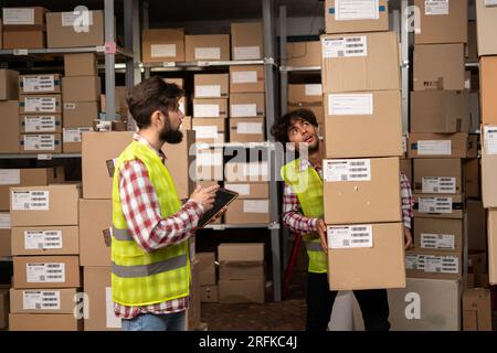 Two warehouse mixed race workers using a digital tablet while recording inventory and preparing shipment. Logistics employees working with warehouse Stock Photo