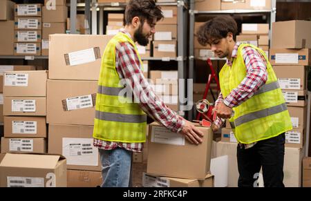 Two warehouse workers sealing cardboard boxes for shipping in a large warehouse Stock Photo