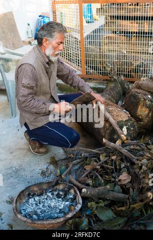 Oct.14th 2022 Uttarakhand, India.Elderly man using a hand axe to cut wooden logs into smaller pieces for firewood in his backyard. Traditional woodcut Stock Photo