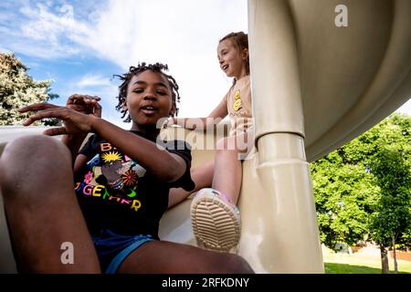 Friends going down slide at park together Stock Photo