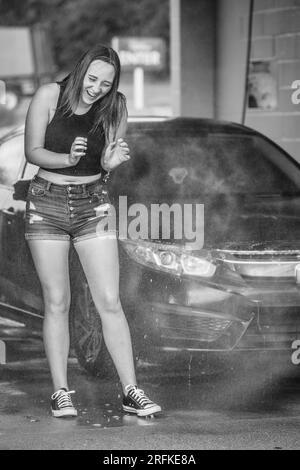 A female getting sprayed with water at the car wash Stock Photo