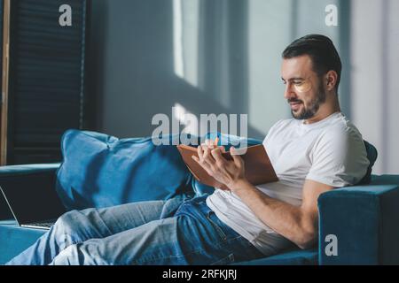 Young man with black hair studying from home writing in a notebook with a pencil, sitting on a sofa. Modern lifestyle. Reading book. Stock Photo