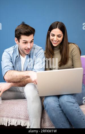 happy young couple sit on couch and using laptop. Cheerful couple smiling and searching on computer Stock Photo