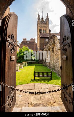 Looking through old medieval wooden doors and archway into a historic brick courtyard with the Palace of Westminster, UK Parliament's Victoria Tower. Stock Photo