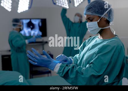 African american female surgeon wearing surgical gown and gloves in operating theatre at hospital Stock Photo