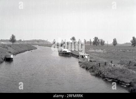 1963, historical, several pleasure or cruise boats moored beside the river on the fens on the Norfolk broads, England, UK. The broads are the UK's largest wetland landscape and a popular place for a boating holiday. Stock Photo