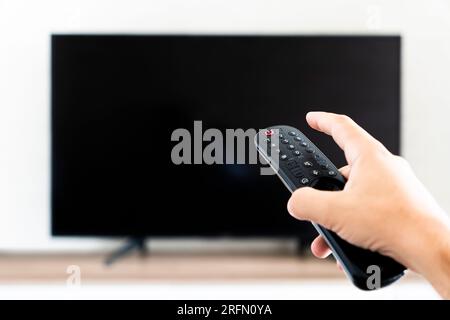 Hand holding remote control for turn off TV. an empty black TV screen. Stock Photo