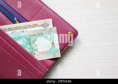 UAE dirham bills in a leather wallet. Fucsia red wallet, purse. Banknotes. Money in cash. Fan of bills. The currency of United Arab Emirates. AED Stock Photo