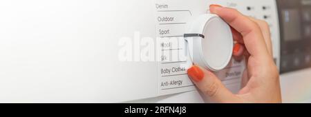 Hands turning on the washing machine close-up. The woman turns on the washing machine and adjusts the duration of the wash. Washing dirty clothes in Stock Photo