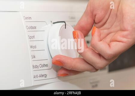 The woman turns on the washing machine and adjusts the duration of the wash. Washing dirty clothes in the washing machine. Hands turning on the Stock Photo