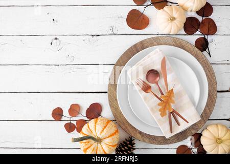 Autumn harvest or thanksgiving dinner table setting with plates, flatware, napkin and fall decor. Overhead view corner border on a white wood backgrou Stock Photo